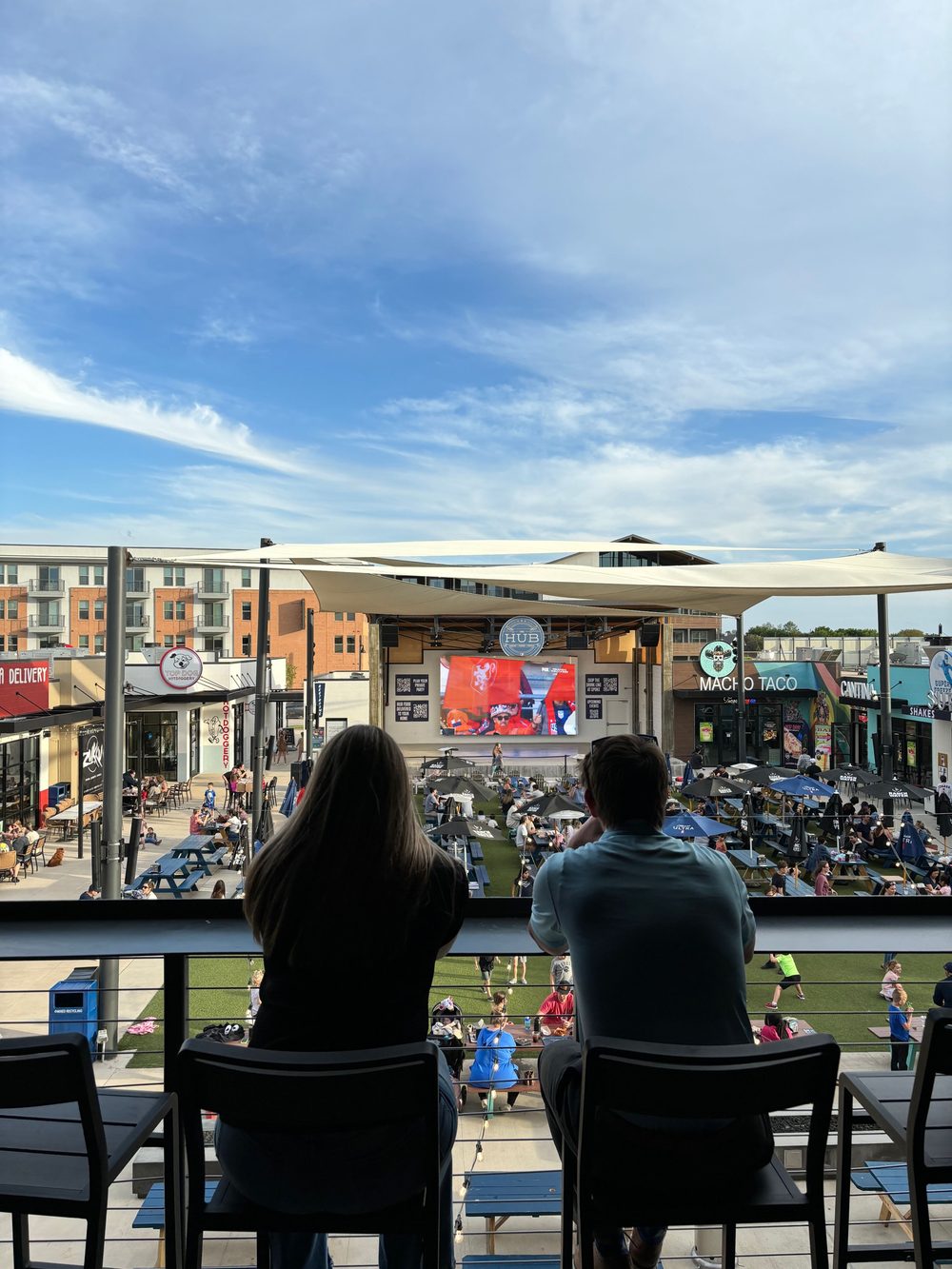 Two people on the upper deck looking out over the packed lawn, the World Cup on the stage screen